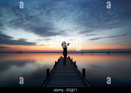 Donna in piedi su una tavola di legno dock presso un lago, ammirando le nuvole in cielo di sera, Steinhude am Meer, Bassa Sassonia Foto Stock