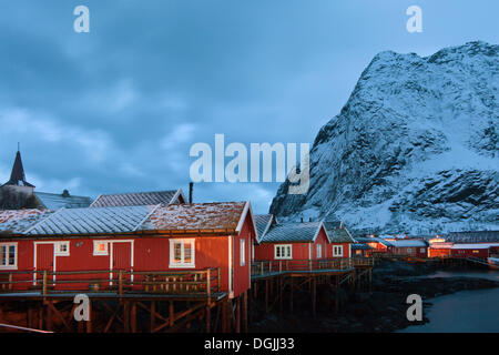 Villaggio di Pescatori con casette rosso accanto a un fiordo in inverno, al tramonto, la Reine, Lofoten, Nordland, Norvegia settentrionale, Norvegia Foto Stock