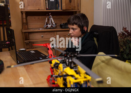 Il ragazzo, 12 anni, guardando un video su un computer portatile con le cuffie, davanti a Lego set di costruzione Foto Stock