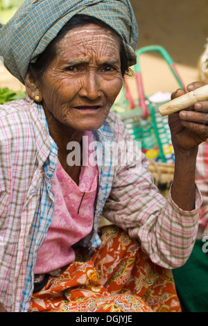 Una vecchia donna di fumare un sigaro di scandaloso in Nyaung oo mercato in Bagan in Myanmar. Foto Stock