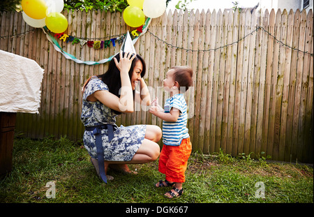 Madre accovacciato mettendo su un partito hat Foto Stock