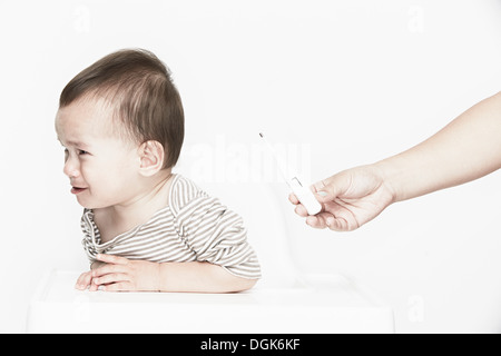 Bambino piange, la mano che regge il termometro digitale Foto Stock