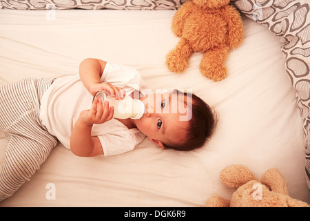 Bambino giacente nella mangiatoia bere il biberon Foto Stock