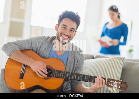 Uomo a suonare la chitarra, donna in background Foto Stock