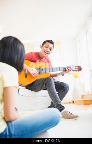 Giovane uomo a suonare la chitarra e cantare, donna ascolto Foto Stock