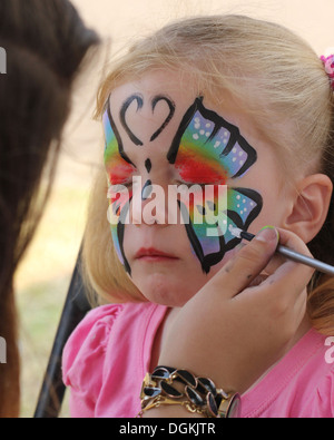 Ragazza bionda ottenendo il suo volto dipinto con una farfalla Foto Stock