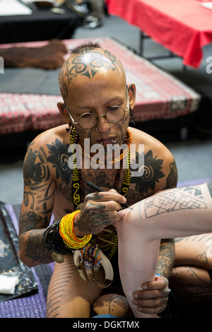 Un tatuaggio indonesiano artista inizia a tracciare un disegno su un uomo del braccio al London International Tattoo Convention. Foto Stock