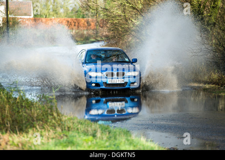 Un blu BMW auto motore aziona attraverso un eccesso di acqua di superficie vicino Billericay Essex dopo un periodo di forti piogge e inondazioni. Foto Stock