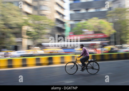 Un uomo in bicicletta sul vuoto del tratto di strada a Mumbai con il traffico intenso di andare nella direzione opposta. Foto Stock