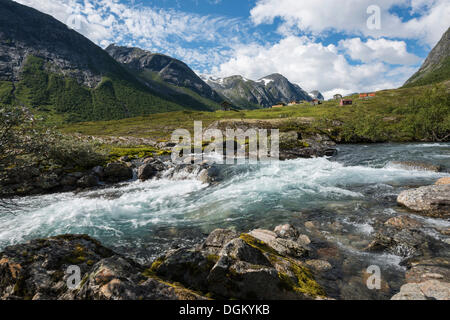 Torrent la formazione di schiuma tra massi di fronte un alm o prato alpino con capanne e montagne, Skjaeringsdalsseter, Grasdal Foto Stock