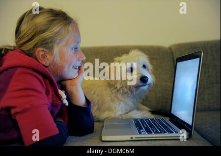 La ragazza con il cane con il computer sul divano Foto Stock