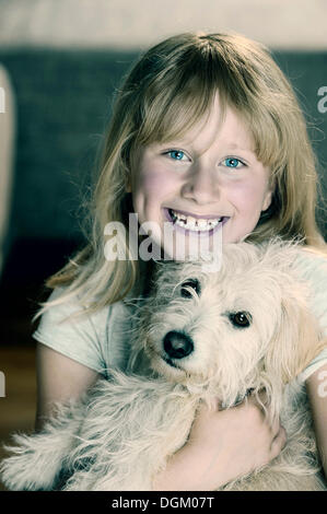 Ragazza, 9, cuddling con un giovane di mixed-cane di razza Foto Stock