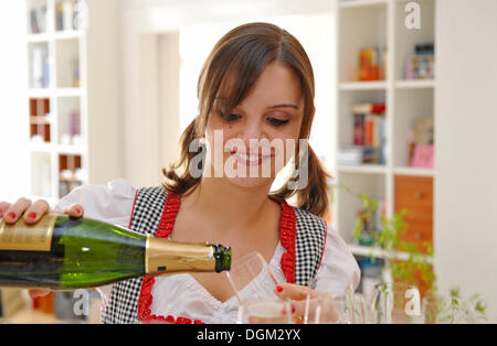 Giovane donna in dirndl, champgane versare in un bicchiere Foto Stock