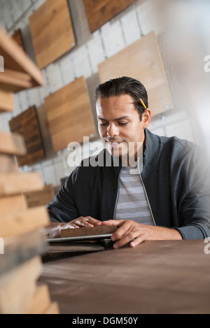 Un giovane uomo in un laboratorio che utilizza materiali riciclati e rigenerati legname a creare mobili e oggetti. Foto Stock