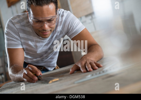 Un giovane uomo in un laboratorio di misura e disegno piani su un bancone. Foto Stock