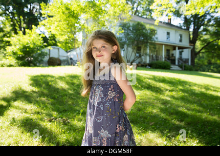 All'aperto in estate. Nella fattoria. Una ragazza in giardino con le mani dietro la schiena.
