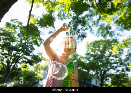 Una giovane ragazza a soffiare bolle in aria sotto i rami di un grande albero. Foto Stock