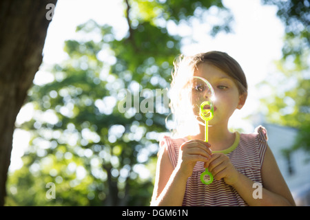 All'aperto in estate. Una giovane ragazza a soffiare bolle in aria sotto i rami di un grande albero. Foto Stock