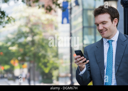 L'estate. Un giovane uomo in un completo grigio e cravatta blu. Utilizzando un telefono intelligente. Foto Stock