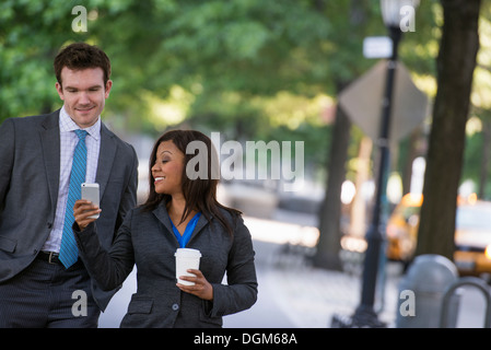 L'estate. Un giovane uomo in un completo grigio e cravatta blu a piedi con una donna in un vestito. L'uomo bianco, nero americano africano donna Foto Stock