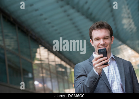 L'estate. Un giovane uomo in un completo grigio e cravatta blu. Utilizzando un telefono intelligente. Foto Stock