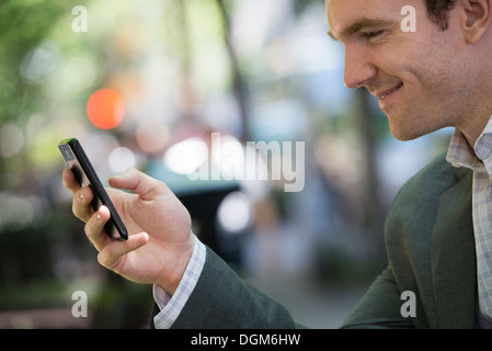 L'estate. Un giovane uomo in un completo grigio. Utilizzando un telefono intelligente. Foto Stock