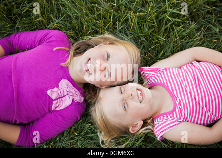 Un ritratto di due sorelle sorridente. Vista dall'alto di due ragazze che giace sulle loro spalle sull'erba, teste insieme. Foto Stock