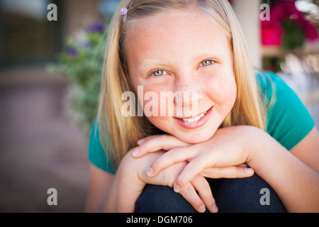 Un bambino, una giovane ragazza seduta inclinato in avanti e sorridente. Il suo mento appoggiato sulle mani. Foto Stock