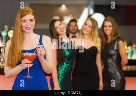 Donna attraente cocktail di tenuta in piedi davanti ai suoi amici Foto Stock