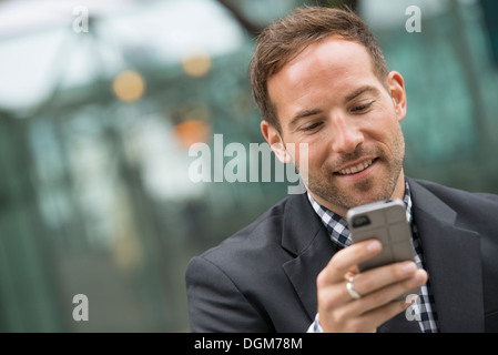 La gente di affari. Un uomo in un business suit. Un uomo con corti capelli rossi e la barba, indossa una tuta, sul suo telefono cellulare. Foto Stock