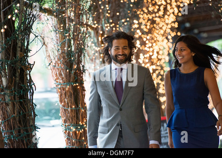 La gente di affari. Due persone, un uomo e una donna si tengono per mano e camminare sotto un pergolato, illuminato con luci fairy. Foto Stock