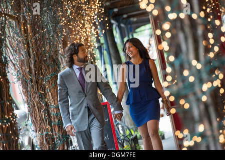 La gente di affari. Due persone, un uomo e una donna si tengono per mano e camminare sotto un pergolato, illuminato con luci fairy. Foto Stock