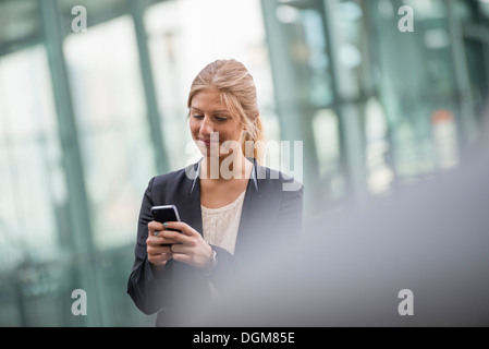 Una bionda e giovane imprenditrice su una città di New York Street. Indossa una giacca nera. Utilizzando un telefono intelligente. Foto Stock