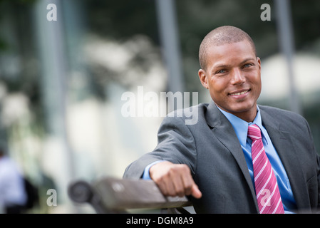 Un giovane uomo in un business vestito con una camicia blu e cravatta rossa Su una strada di città. Sorridente alla fotocamera. Foto Stock