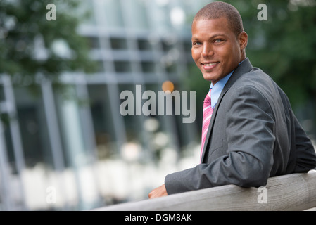 Un giovane uomo in un business vestito con una camicia blu e cravatta rossa Su una strada di città. Sorridente alla fotocamera. Foto Stock