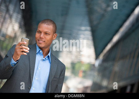 Un imprenditore in un vestito con il suo collare della camicia rimosse. In una New York City street. Utilizzando un telefono intelligente. Foto Stock