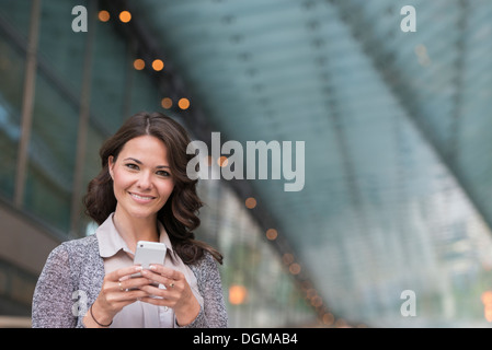 La gente di affari. Una imprenditrice in una leggera giacca grigia, utilizzando il suo smart phone. Foto Stock