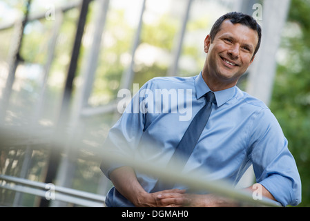 La gente di affari esterni. Un imprenditore di latino in camicia e cravatta, poggiando su una ringhiera. Rilassante. Foto Stock