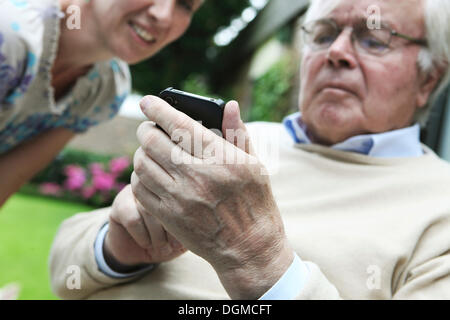 Giovane donna spiegando a un senior citizen come utilizzare uno smartphone Foto Stock