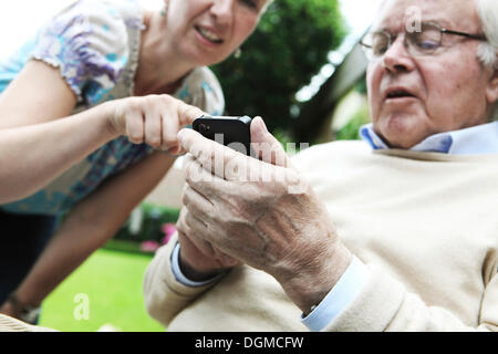 Giovane donna spiegando a un senior citizen come utilizzare uno smartphone Foto Stock