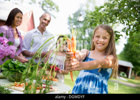 Festa di famiglia. Una tabella di cui con insalate e frutta fresca e verdura bambino tenendo fuori freschi carote prelevate. Foto Stock