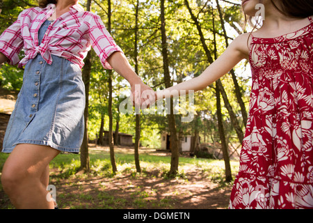 Una donna e una giovane ragazza tenendo le mani e che corre lungo sotto gli alberi.