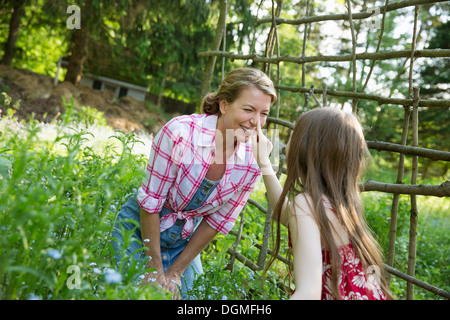 Madre e figlia insieme in un contenitore di piante in un giardino. Verde piante frondose. Un bambino di toccare la donna adulta del naso. Foto Stock