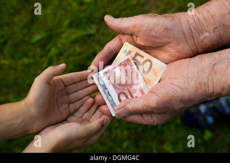 Donna anziana dando un bambino denaro, le banconote in euro Foto Stock