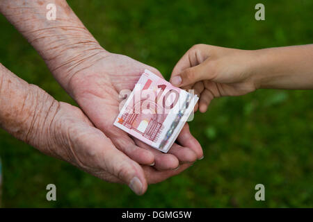 Bambino dando una donna anziana a dieci banconote in euro Foto Stock