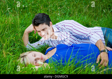 Uomo disteso con la sua donna incinta in erba e guardando il suo teneramente Foto Stock