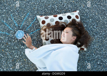 Giovane donna in appoggio la sua testa su un cuscino, giacente sul suolo coperto con una coperta, colpendo dipinto sveglia squilla Foto Stock