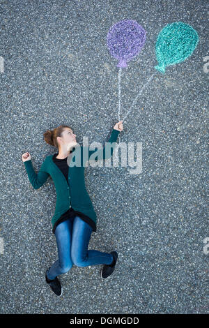 Giovane donna appaiono essere sospesi da due palloncini verniciato, presa da sopra Foto Stock