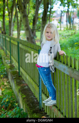 Ragazza 4 anni, appoggiata contro una recinzione di legno Foto Stock