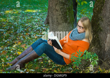 Giovane donna con gli occhiali seduto nel parco e la lettura di un libro Foto Stock